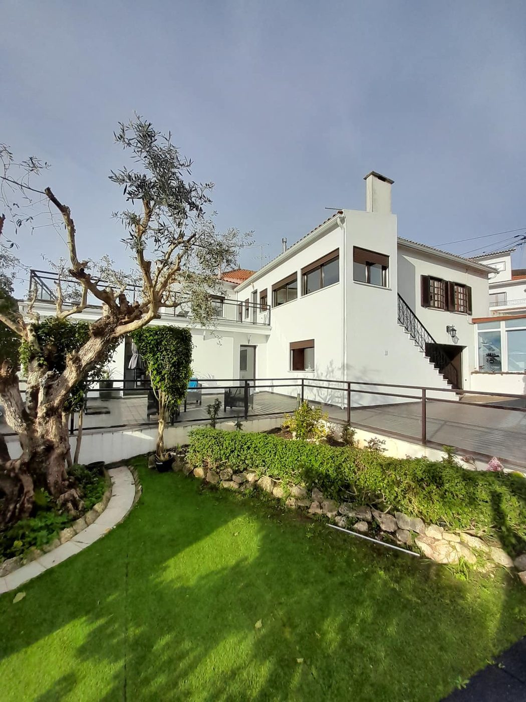 Fachada branca da casa com oliveiras no jardim