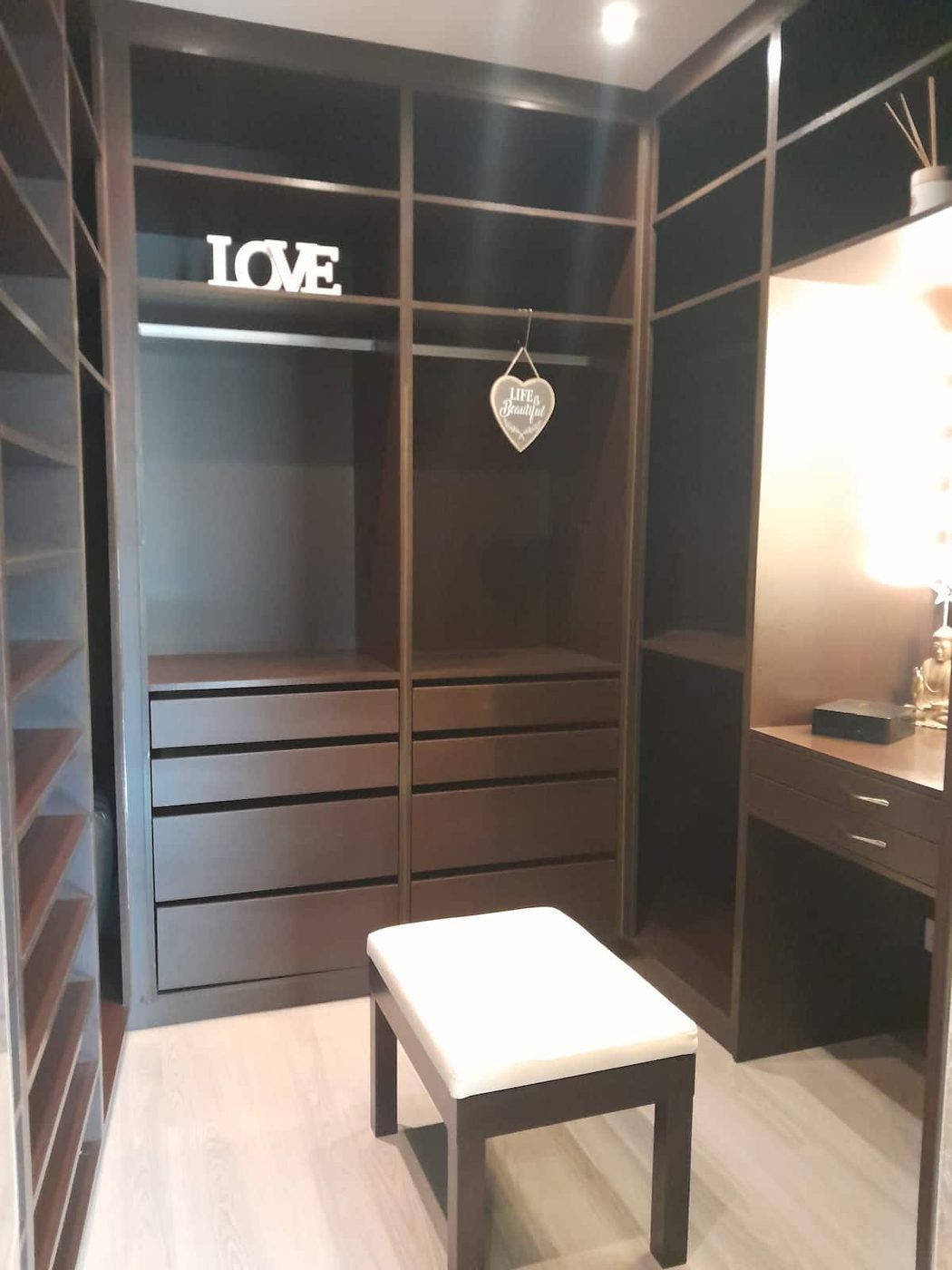 Closet em madeira escura com gavetas, espelho e banco branco