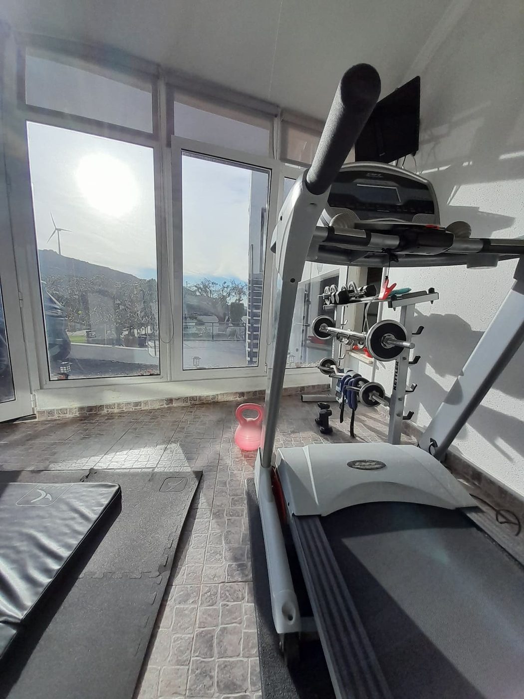 Ginásio com passadeira e pesos junto a janelas amplas com vista para a serra