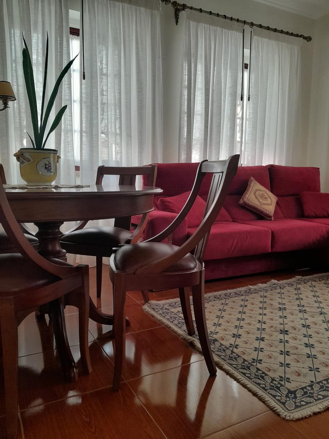 Sala de jantar com mesa de madeira, cortinas brancas e sofá vermelho