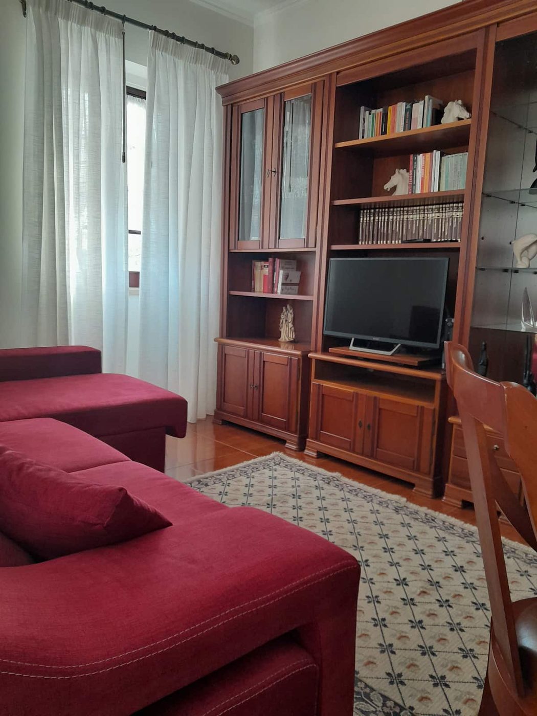 Sala de estar com sofás vermelhos, estante de madeira e TV